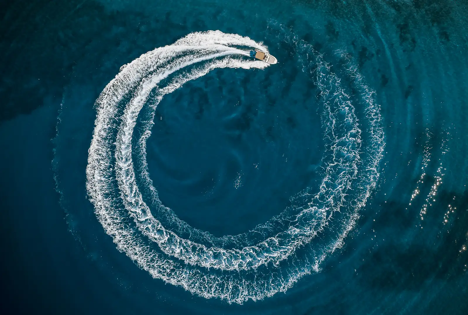 Aerial view of a speedboat carving a circular wake in dark blue water