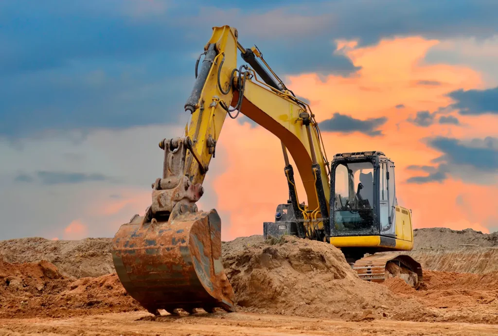 Excavator digging in sandy ground at sunset