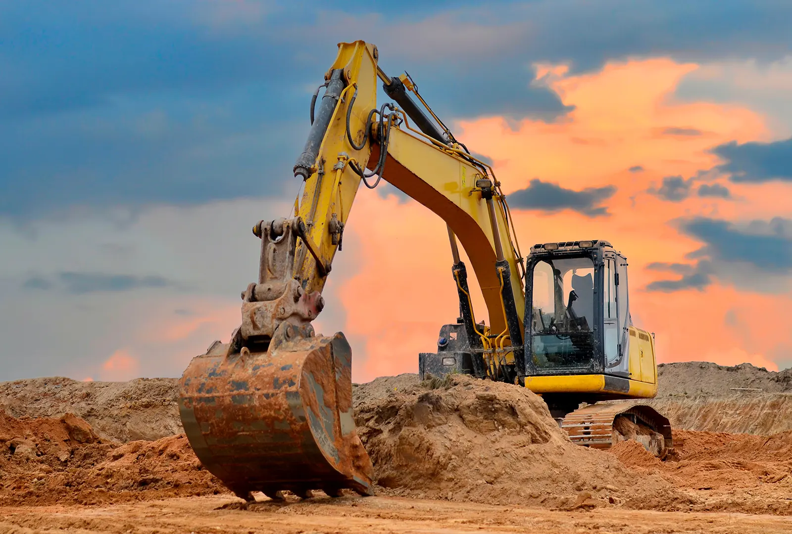 Excavator digging in sandy ground at sunset