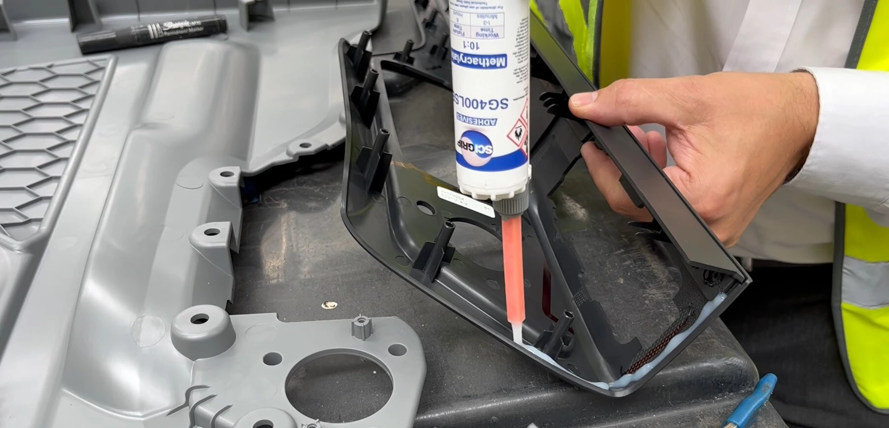 Worker bonding a black plastic bracket to a vehicle panel