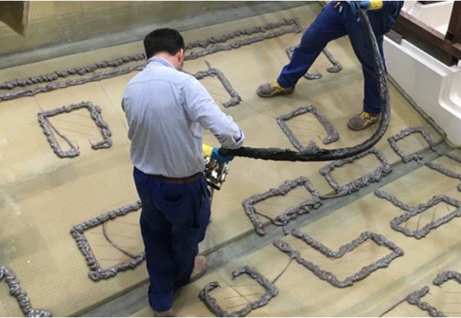 Worker applying beads of adhesive in a grid pattern on a boat deck
